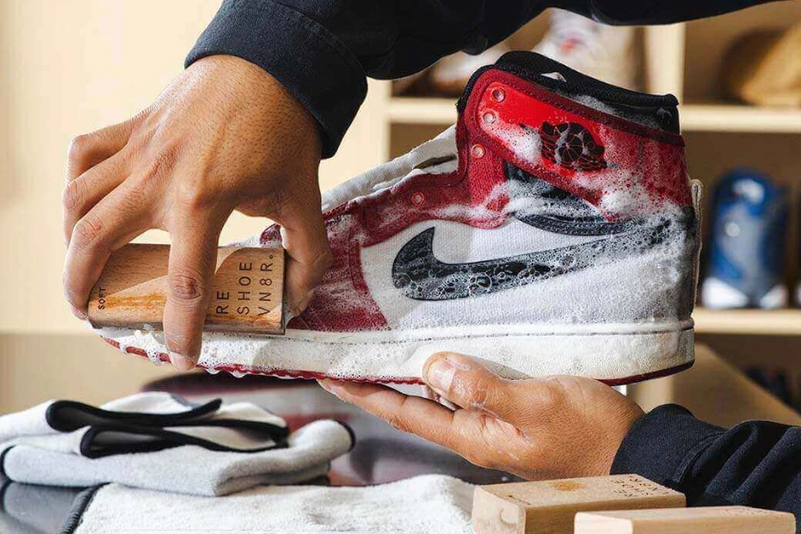 Individual cleaning a red, white, and black Air Jordan 1 sneaker with a brush and foaming solution at a Downingtown, PA sneaker care store.​